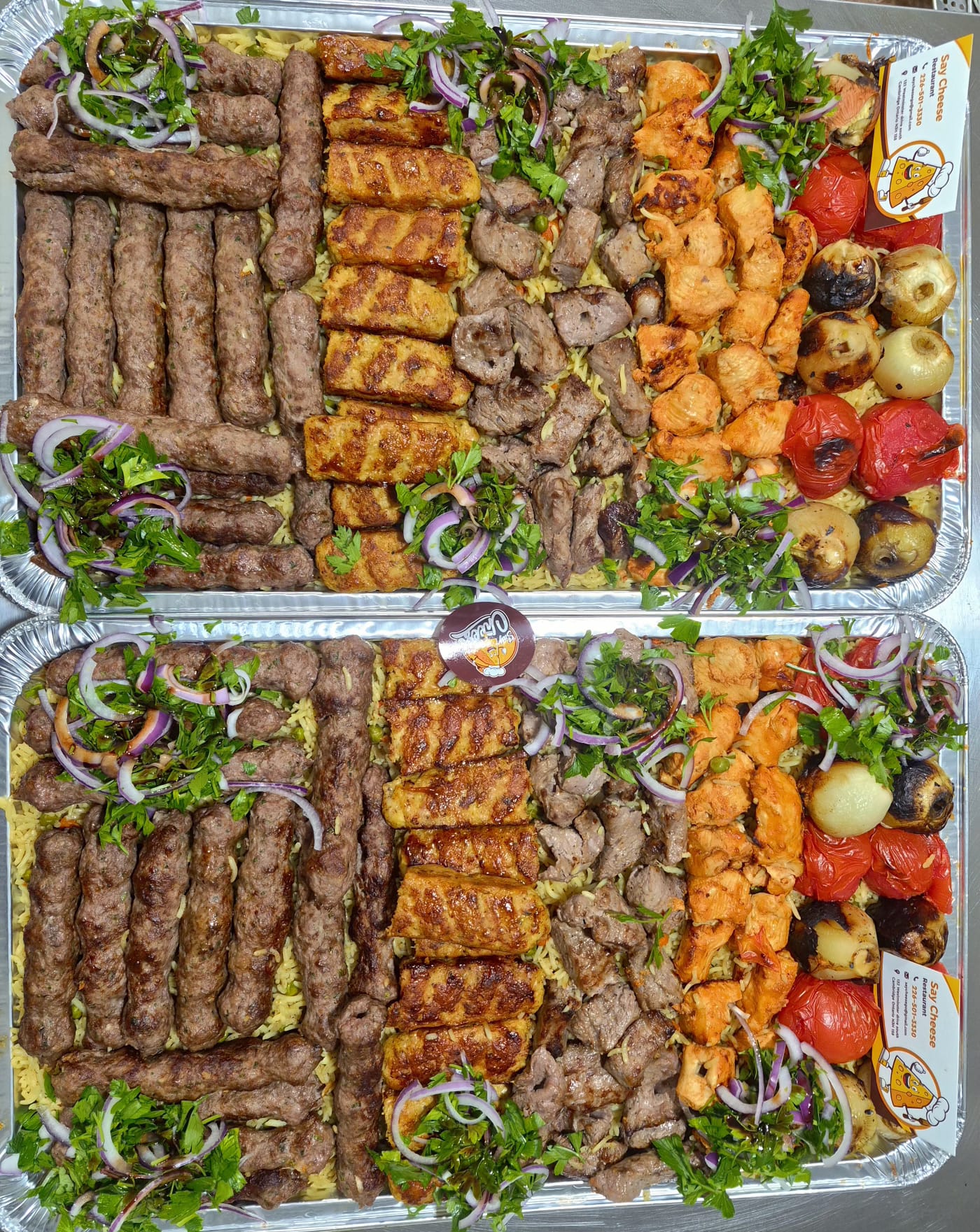 Two generous Say Cheese catering trays loaded with grilled kebab, shish taouk, kafta, rice and roasted vegetables